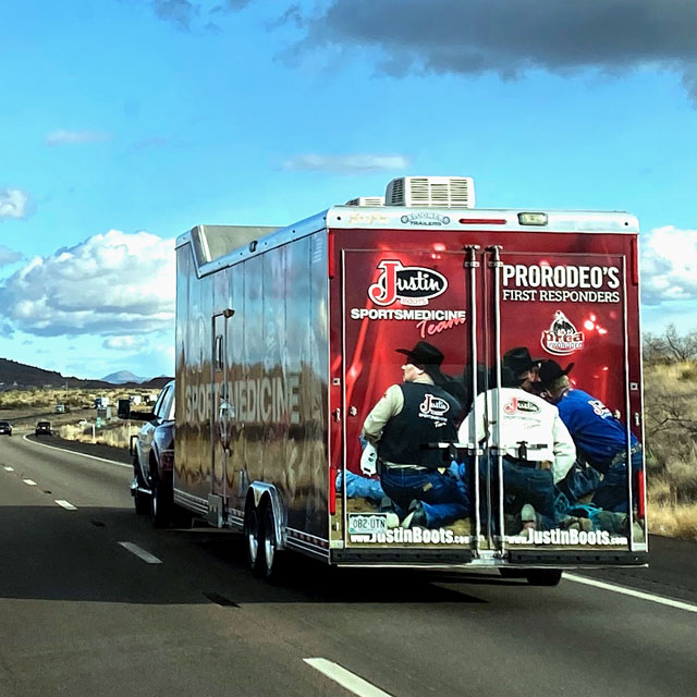 A red, black and white trailer driving away from the camera into the blue skies on the road.